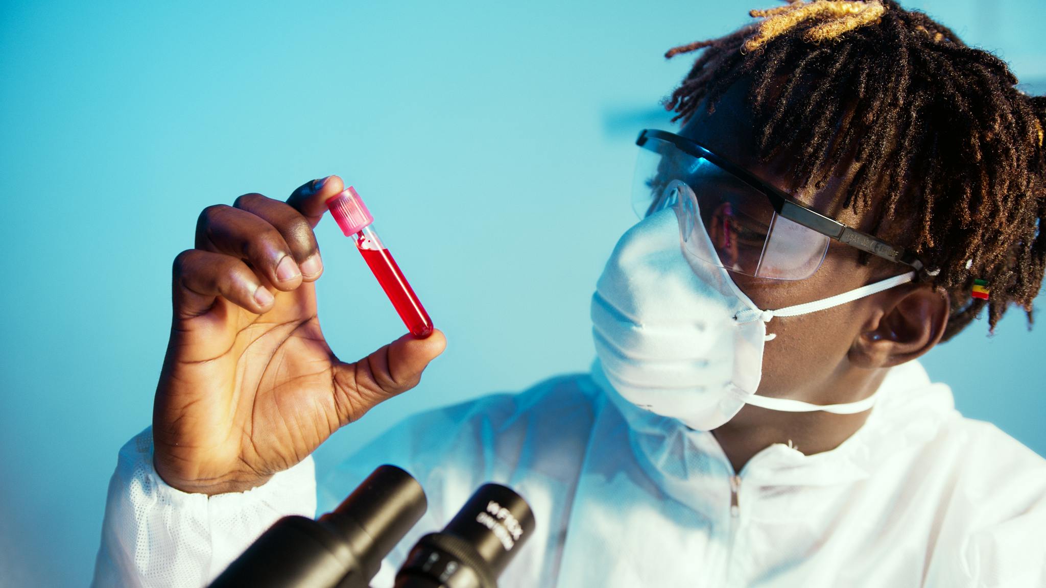 Scientist wearing PPE examining blood sample in a laboratory setting.
